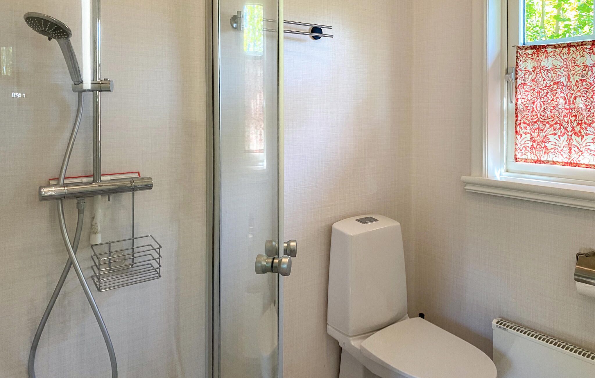 Een badkamer met een glazen douchecabine, toilet en een raam met decoratieve gordijnen.