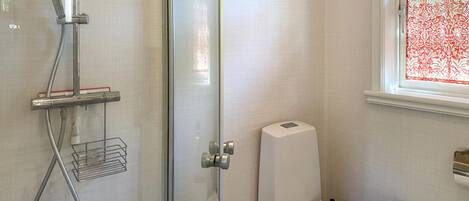 Een badkamer met een glazen douchecabine, toilet en een raam met decoratieve gordijnen.