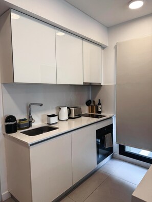 Een moderne keuken met witte kastjes, een roestvrijstalen spoelbak, een waterkoker, een broodrooster en een fles wijn.