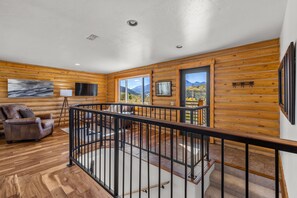 A wooden cabin interior with a living area, a balcony with a view, and a mounted television. - 5 Bedroom Log Cabin with Beautiful Mountain Views - Nearby Resorts (Silverthorne)