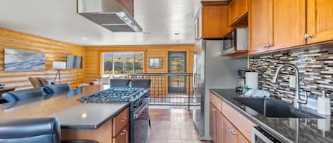 A modern kitchen with wooden cabinetry, a gas stove, a refrigerator, and a large window offering a view of the outdoors.