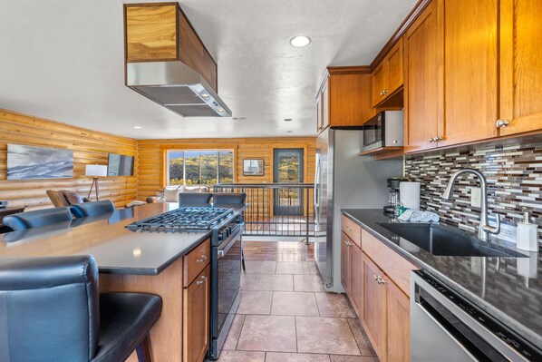 A modern kitchen with wooden cabinetry, a gas stove, a refrigerator, and a large window offering a view of the outdoors.