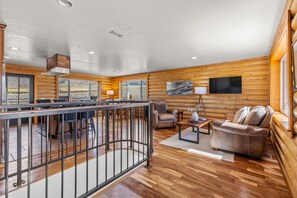 A spacious living area with a wooden floor, a seating arrangement, a television, and a view of the outdoors. - 5 Bedroom Log Cabin with Beautiful Mountain Views - Nearby Resorts (Silverthorne)