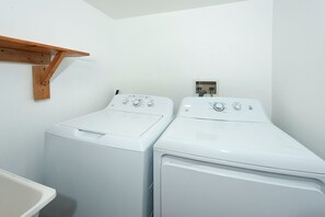 A laundry room with two white front-loading washing machines and a wooden shelf above them. - 5 Bedroom Log Cabin with Beautiful Mountain Views - Nearby Resorts (Silverthorne)