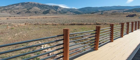 Um deck de madeira com guarda-corpo metálico com vista para uma paisagem montanhosa.