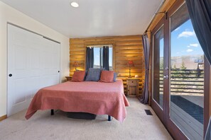 A bedroom with a bed, a nightstand, a window with curtains, and a view of the outdoors. - 5 Bedroom Log Cabin with Beautiful Mountain Views - Nearby Resorts (Silverthorne)