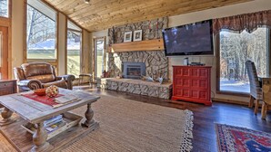 A spacious living room with a stone fireplace, a large flat-screen TV, leather chairs, and a wooden coffee table. - Serene Ski Retreat w/Elkhorn in SV amenity pass! (Sun Valley)