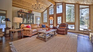 A spacious living room with a large window, a leather sofa, a wooden coffee table, and a chandelier. - Serene Ski Retreat w/Elkhorn in SV amenity pass! (Sun Valley)