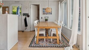 A dining area with a wooden table and white chairs, a woven pendant light, and a patterned rug. - 5 Star Holiday Home in Dronningmolle (Dronningmolle)