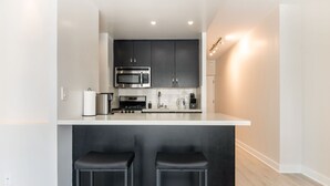 A modern kitchen with dark cabinets, a white countertop, two bar stools, and a microwave.