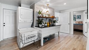 A laundry room with a washing machine, a drying rack, and a shelf with plants and decorative items.