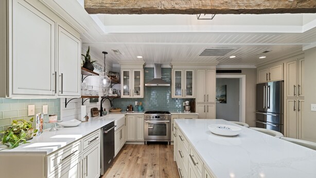 A spacious kitchen with white cabinetry, a large island, and a wooden floor.