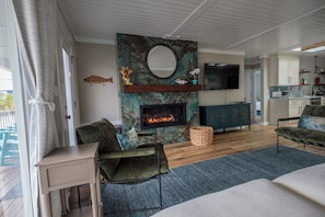 A living room with a fireplace, a television, and a kitchen area in the background.