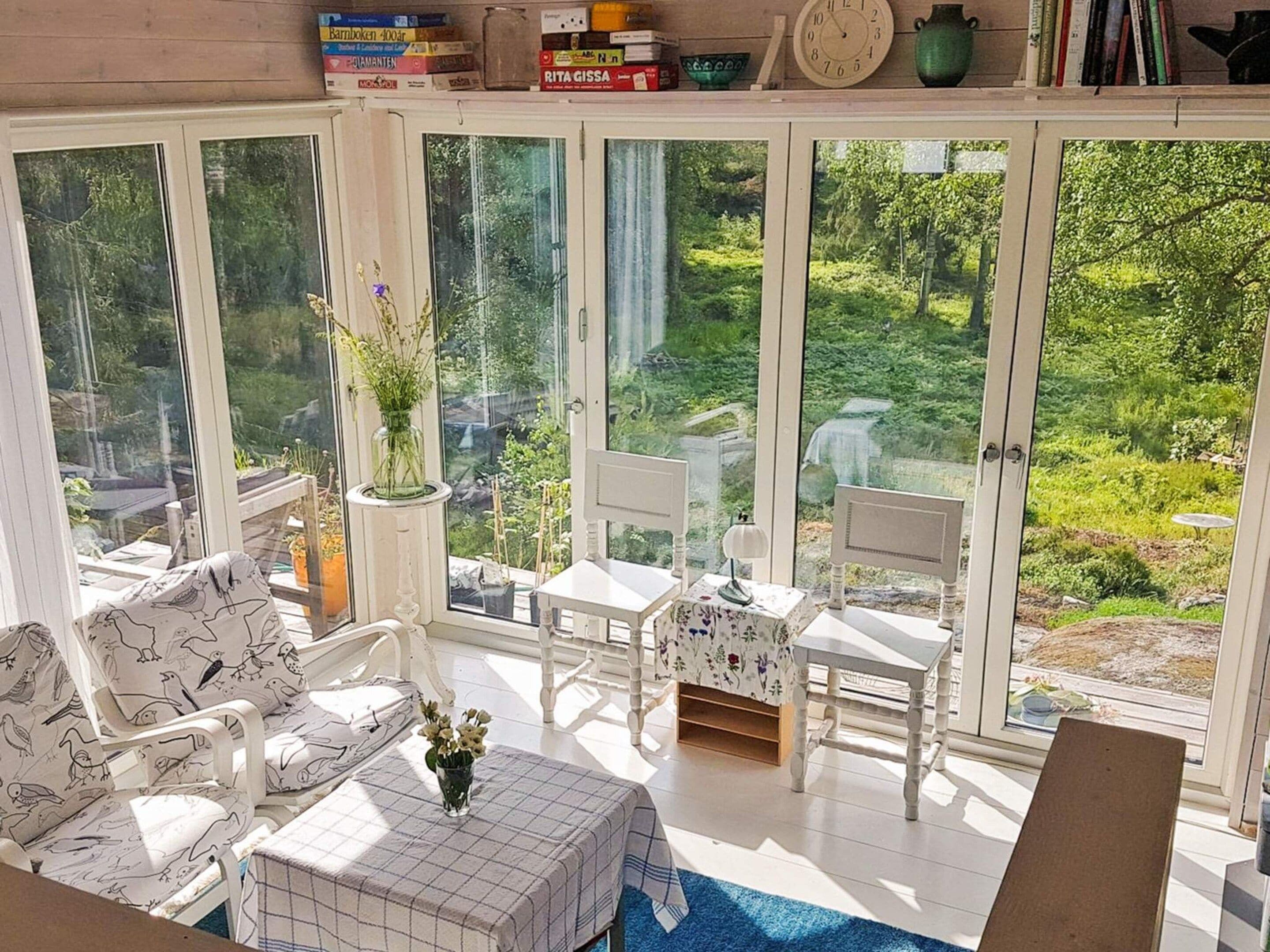 Quarto iluminado pelo sol com vista para um jardim exuberante, móveis brancos e uma estante de livros.