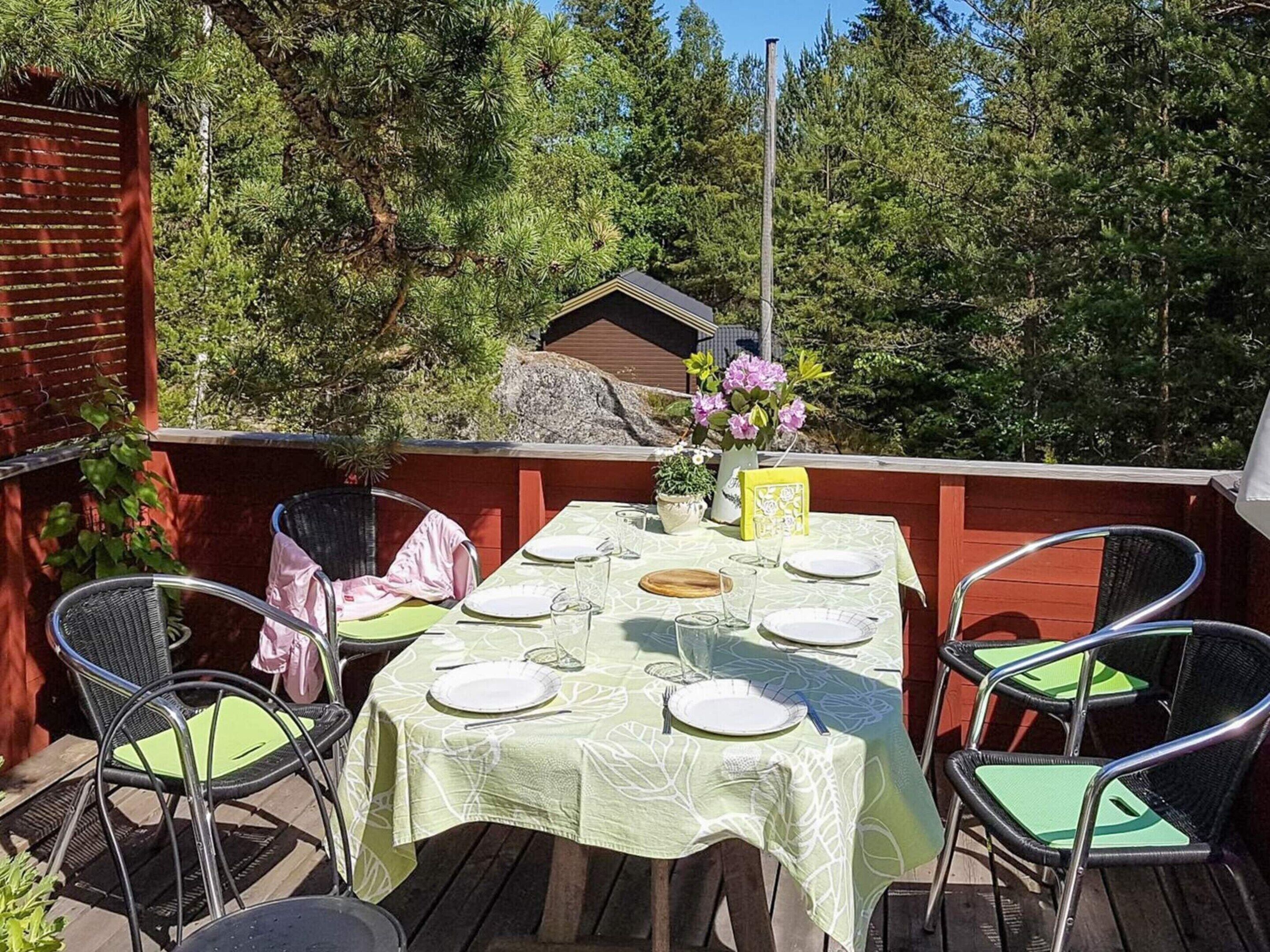 An outdoor dining area with a table set for four, surrounded by chairs with green cushions.