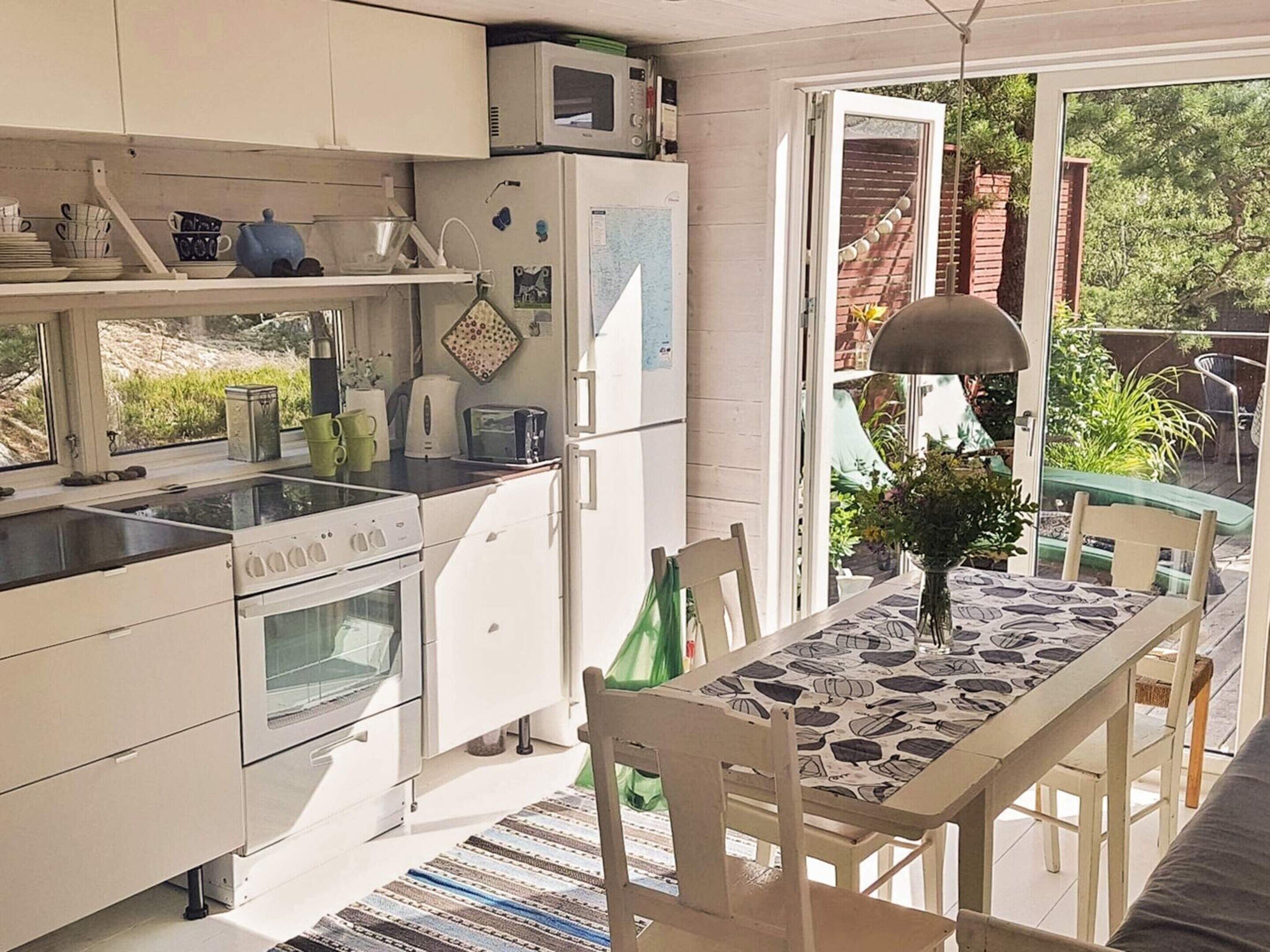 Una cucina compatta con mobili bianchi, un fornello e un frigorifero. C'è un tavolo da pranzo con sedie e una vista sul giardino tramite una porta vetrata.