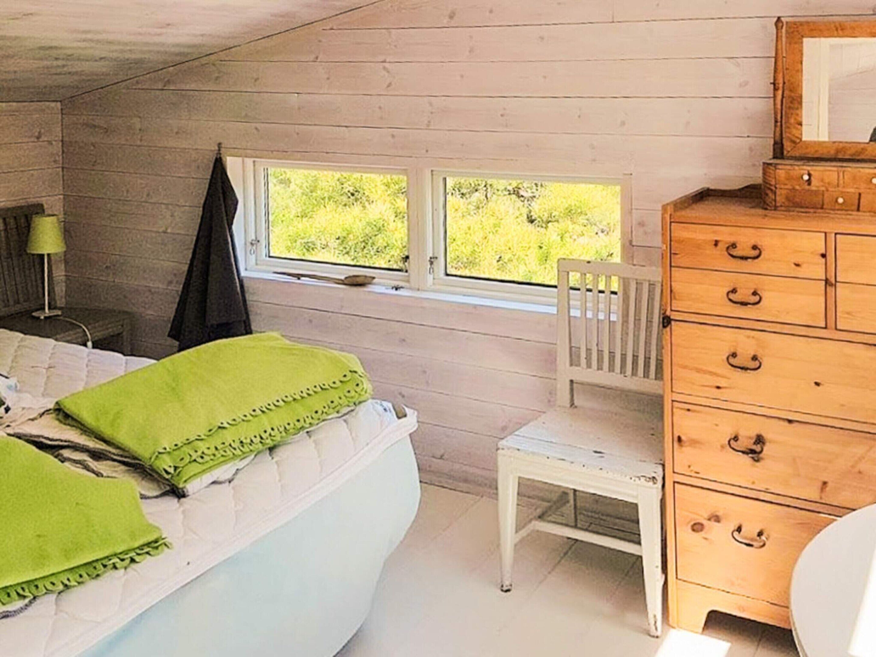 Una camera da letto con un letto, una cassettiera in legno, una sedia, una finestra e una lampada.