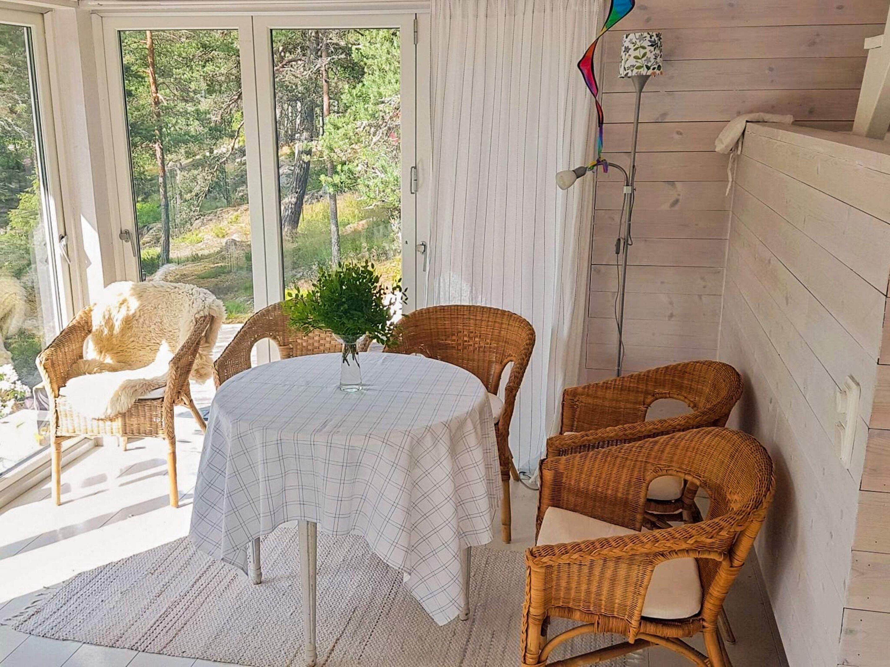 A room with a round table, wicker chairs, a potted plant, and a view of trees through a glass door.