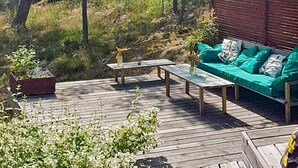 A wooden deck with a green sofa and a small table, surrounded by plants and trees. - 4 Star Holiday Home in Stavsnas (Stavsnäs)