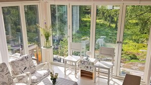 A sunlit room with large windows, white furniture, and a view of a lush garden. - 4 Star Holiday Home in Stavsnas (Stavsnäs)