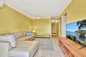 A living room with a beige sofa, a patterned rug, and a television displaying a coastal view.