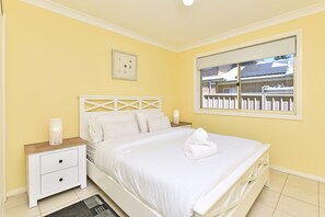 A bedroom with a bed, nightstands, a window with a view, and a wall-mounted light fixture.