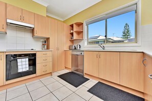 A modern kitchen with wooden cabinets, a built-in oven, and a window with a view of houses.