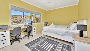 Un dormitorio con cama, escritorio, silla, computadora y vistas al exterior.