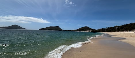 Una playa con aguas cristalinas, una orilla arenosa y colinas a lo lejos.