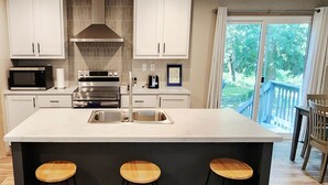 A modern kitchen with white cabinets, a large island with stools, stainless steel appliances, and a view of a balcony. - 3-bedroom house in delightful Hilton Head Island, SC (Hilton Head Island)