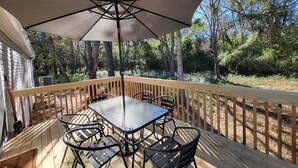 A wooden deck with a table and chairs, an umbrella, and a view of trees and a house. - 3-bedroom house in delightful Hilton Head Island, SC (Hilton Head Island)