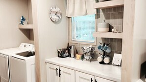 A laundry area with a washing machine, a drying rack, a clock, and a window with blinds. - 3-bedroom house in delightful Hilton Head Island, SC (Hilton Head Island)