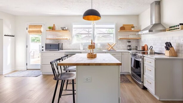 A modern kitchen with a central island, white cabinetry, and a black pendant light.