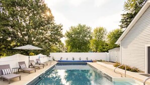 A rectangular swimming pool with a blue edge, surrounded by lounge chairs and a white fence.