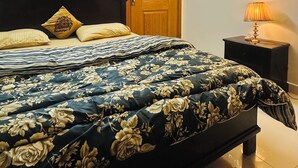 Ein Schlafzimmer mit einem Bett, einem Deckenventilator, einer Holztür, einem Nachttisch mit Lampe und einer Wandleuchte.