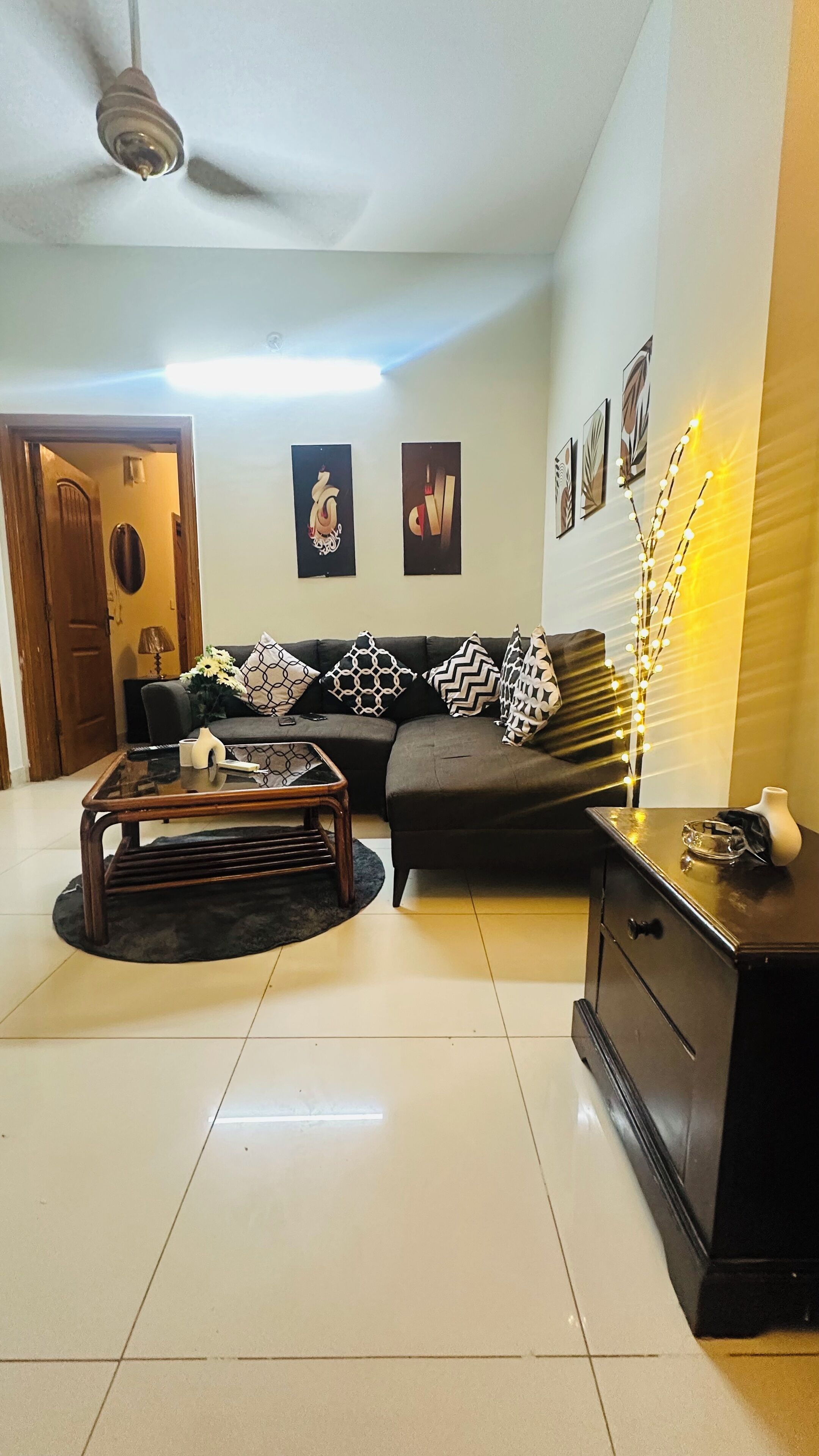 A living room with a sofa, coffee table, and decorative items. There is a door and a wall with framed pictures.