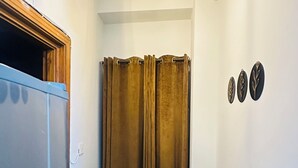 Un couloir étroit avec un meuble bleu, un rideau marron, une plante en pot et trois éléments décoratifs fixés au mur.