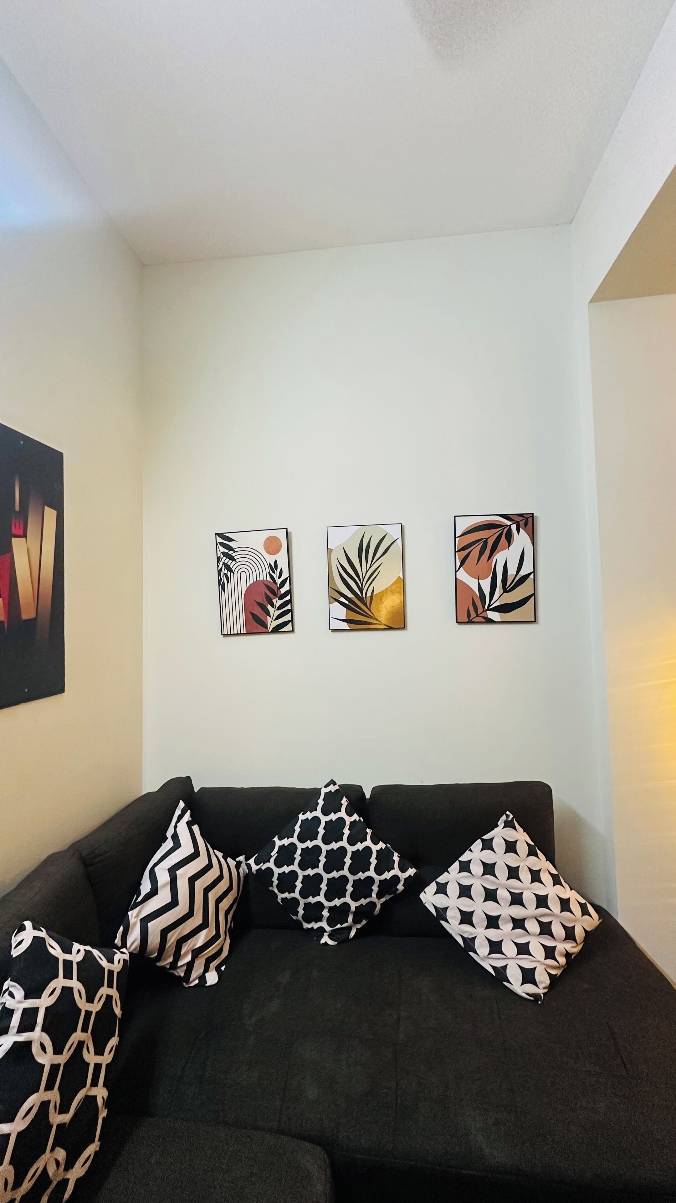 A living room with a black sofa, three abstract paintings on the wall, and a large abstract painting on the left.
