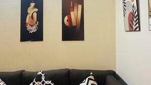 Un salon avec un canapé gris foncé, des coussins à motifs et trois œuvres d’art encadrées accrochées au mur.