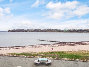 A beach with a lifebuoy sign, a pier, and a circular table with benches in the foreground.