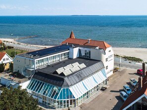 A coastal building with a glass conservatory, a red-roofed section, and a view of the sea.