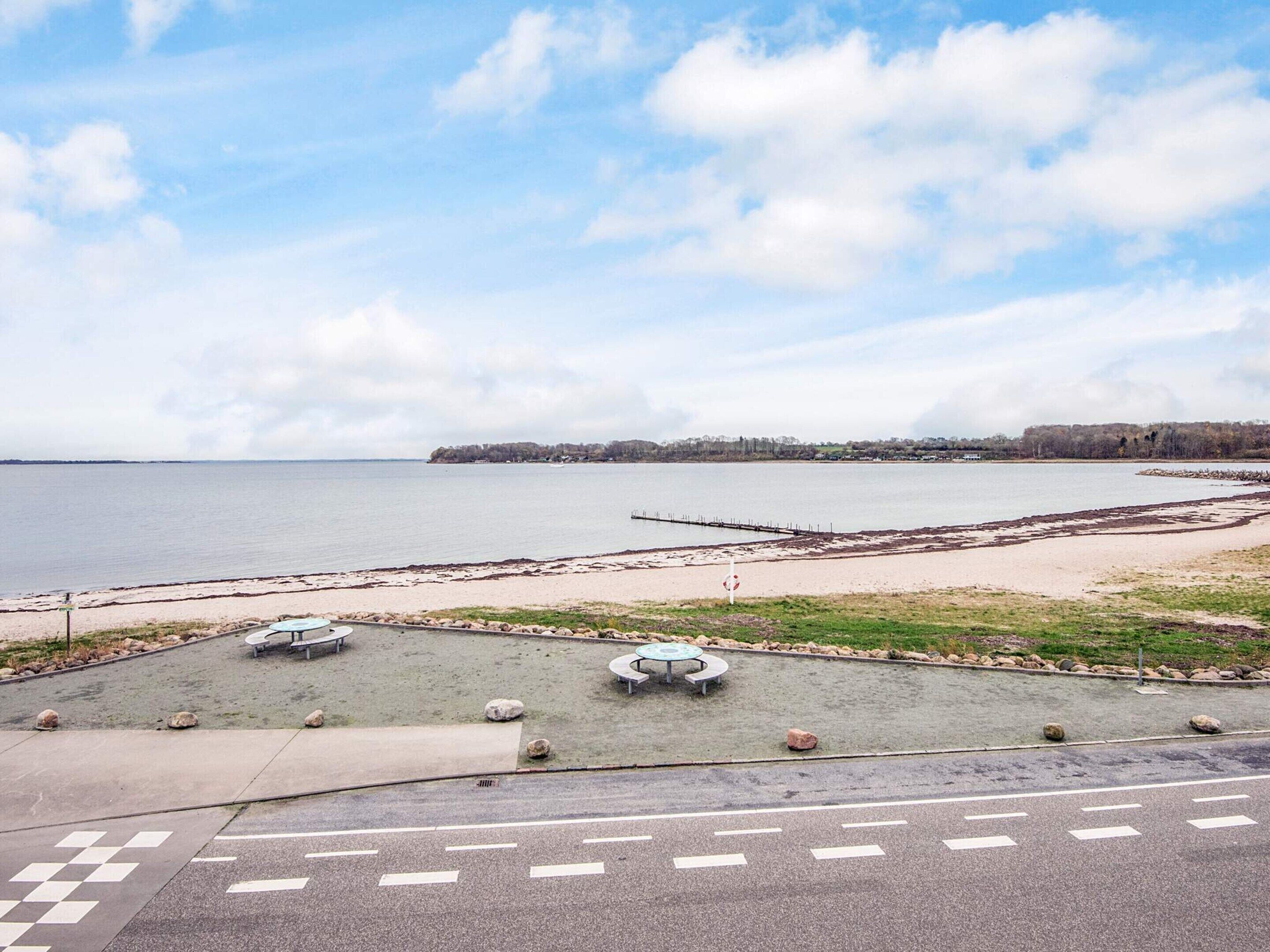 Un parc au bord de l’eau, doté de bancs et d’un espace de repos circulaire, d’une promenade pavée et offrant une vue sur l’eau et les bâtiments situés au loin.
