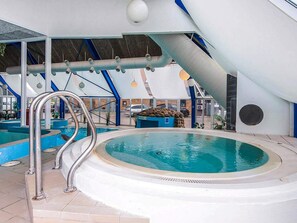 An indoor swimming pool with a circular shape, surrounded by a white tiled floor and a blue pool deck.