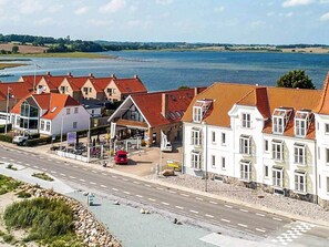 A coastal town with a row of white buildings with red roofs, a road in the foreground, and a body of water in the background.