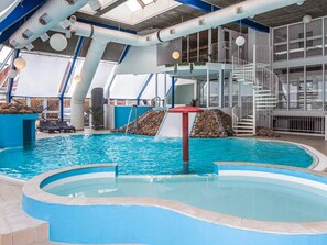 An indoor swimming pool with a slide, a staircase, and lounge chairs.
