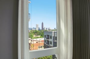 Une vue sur la ville, avec ses bâtiments, à travers une fenêtre, sous un ciel dégagé.