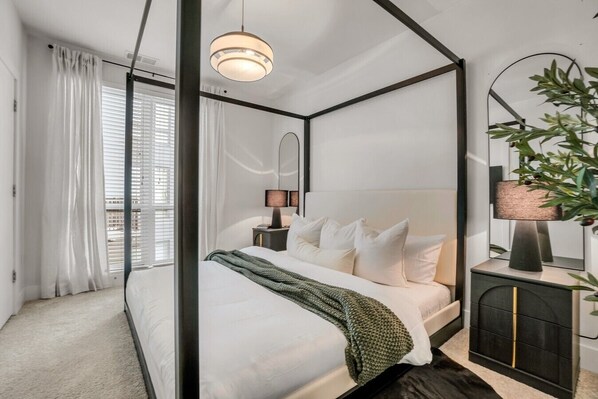 A bedroom with a four-poster bed, a bedside lamp, a mirror, and a potted plant.