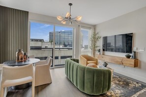 Ein modernes Wohnzimmer mit Essbereich, einem grünen Sofa, einem Holztischchen und einem großen Fenster mit Blick auf die Stadt.