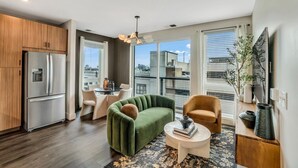 Un salon moderne avec un canapé vert, un fauteuil marron, une table basse ronde et un coin repas comprenant une table et des chaises.