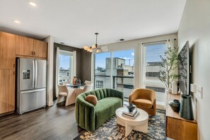 Eine moderne Wohnung mit Küche, einem grünen Sofa, einem kleinen runden Tisch und einem Balkon mit Blick auf die Stadt.